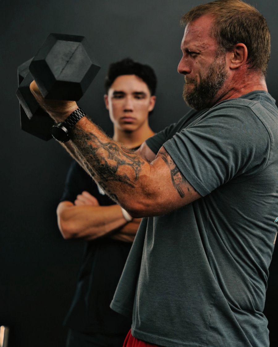 Client curling a heavy dumbbell while his coach watches